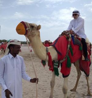 човек који стоји поред особе која јаше камилу