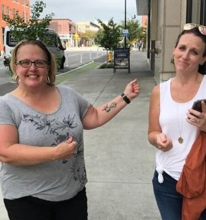 两名女子站在人行道上，手里拿着手机