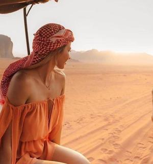 一位身穿橙色连衣裙的女子和一只山羊坐在沙漠中