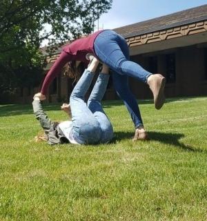 草地上，一名女子站在另一名男子的身上