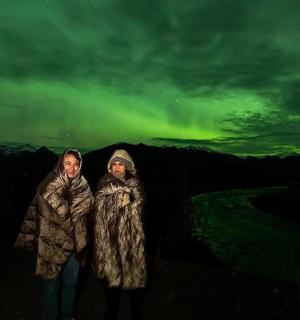 a couple of people standing under the northern lights