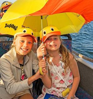 two girls sitting on a boat holding an umbrella