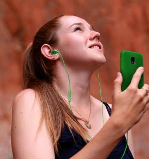 mladá žena se sluchátky na uších dívá se na svůj mobilní telefon