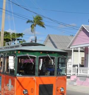 an orange and green trolley driving down a street with a lighthouse