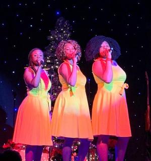 tři ženy zpívající na pódiu s vánočním stromečkem