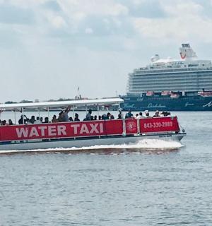 a red water taxi boat in the water with a cruise ship