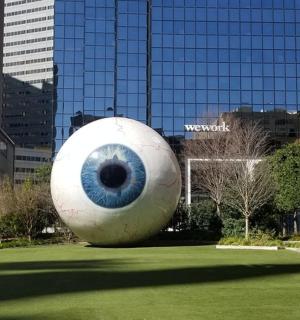 a large eyeball statue in a field with a city