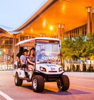 skupina lidí jedoucích po ulici v golfovém vozíku