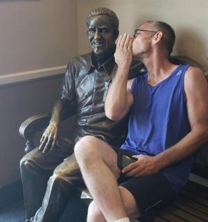 muž sedící na lavičce vedle sochy