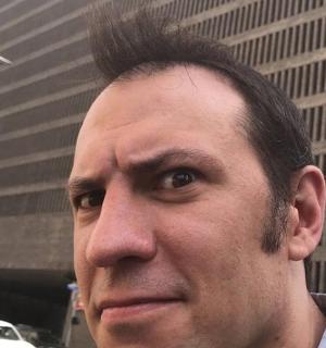 muž s vlasy na hlavě před budovou