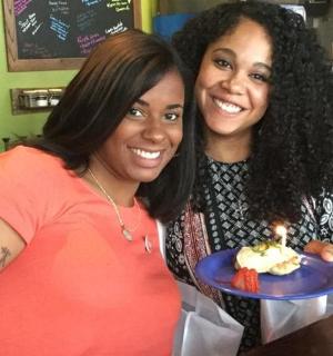 两个女人拿着盘子，盘子里放着一根蜡烛的蛋糕