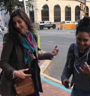two women are walking down the street looking at their cell phones