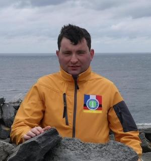 muž ve žluté bundě sedící na skalách u oceánu