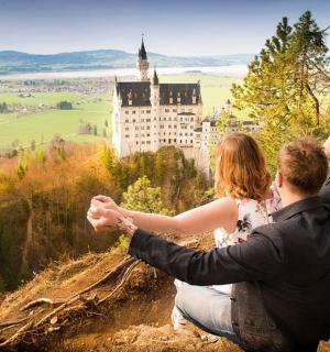 a man and a woman sitting on a rock in front of a castle