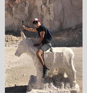 一名男子坐在一名骑马男子的雕像上