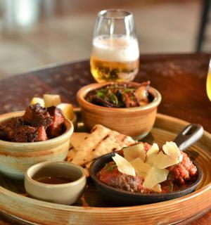 a table with a plate of food and two glasses of beer