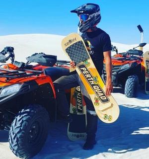 Muž sedící na čtyřkolce v písku se snowboardem