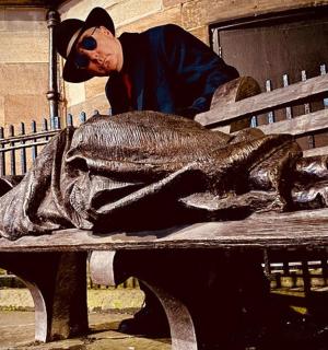 一名男子站在长椅上的鱼雕像旁边