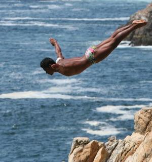 muž skákající z útesu do oceánu