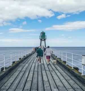 a group of people walking on a pier with a lighthouse