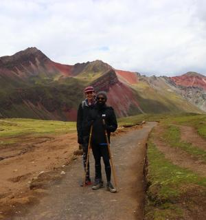 two people standing on a dirt road with mountains in the background