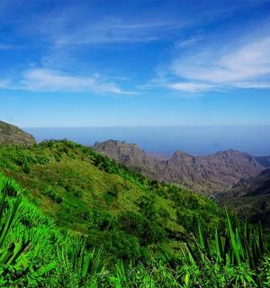a view of a green mountain with mountains in the background