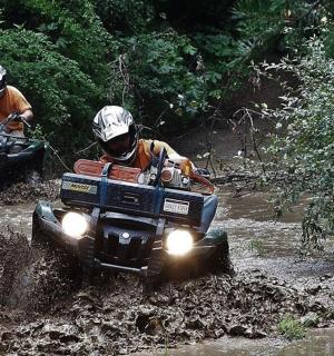 zwei Personen fahren auf Geländefahrzeugen im Schlamm
