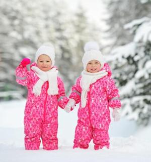 Dvě děti v růžových pyžamech se drží za ruce ve sněhu