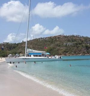 muž stojící ve vodě na pláži s plachetnicí