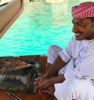 一名男子坐在水边的烤架旁