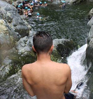 a shirtless man standing in front of a waterfall