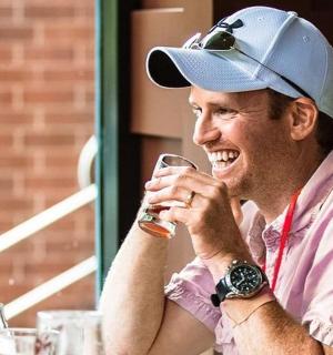 a man wearing a hat drinking a glass of wine