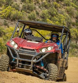 两个人骑着一辆红色的全地形车在土路上行驶