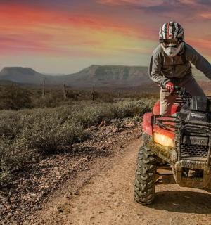 two people riding on a four wheeler on a dirt road