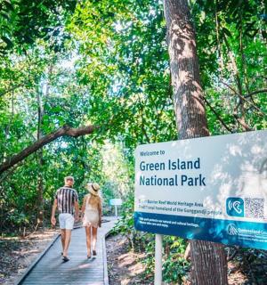 a man and woman walking on a wooden path next to a sign