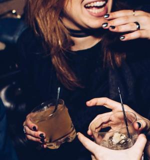 two women laughing while holding drinks in their hands