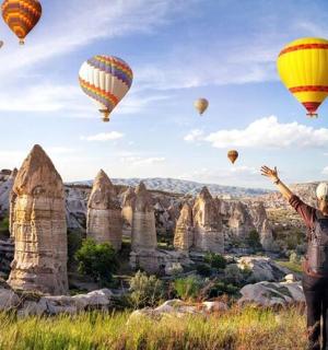 a person standing in a field watching hot air balloons