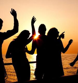 skupina lidí stojící na pláži při západu slunce