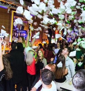 eine Gruppe von Leuten steht in einer Bar und wirft Papiere in die Luft