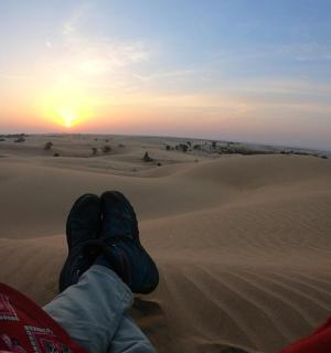 člověk sedící v poušti a pozorující západ slunce