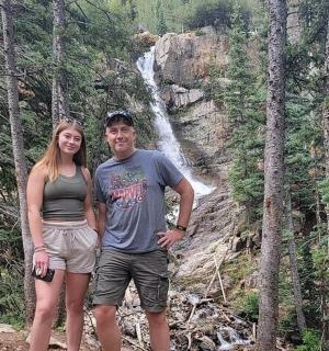 a man and a woman standing in front of a waterfall