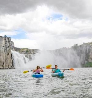 divi cilvēki kajakos ūdenī ūdenskrituma priekšā