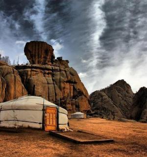 a yurt in a field next to a rock formation