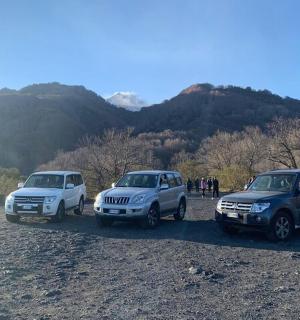 three vehicles parked next to a river with mountains in the background