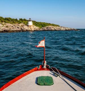 a boat with a flag on the water with a lighthouse