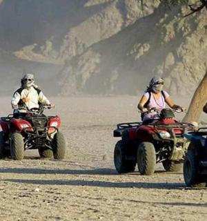 三个人骑着四轮摩托车在沙漠中行驶