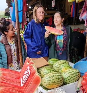 a group of women standing around a market with watermelon