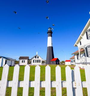 a white picket fence with a lighthouse behind a house