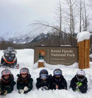 skupina lidí sedících ve sněhu před cedulí