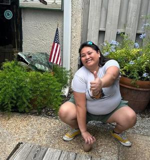 a woman giving a thumbs up while kneeling in front of a house